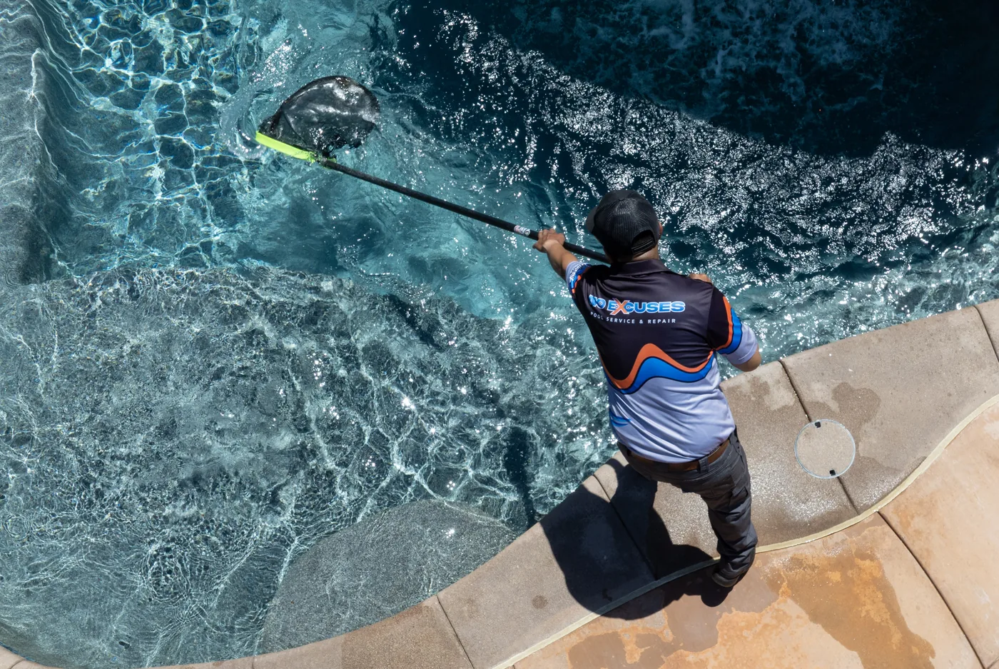 Pool technician skimming pool from overhead — No Excuses Pool Service